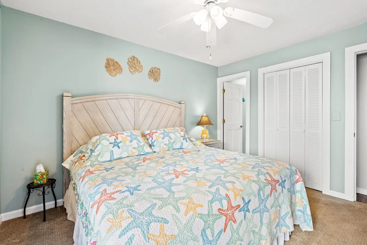 This image features a bed adorned with a starfish-patterned quilt, a nightstand with a lamp, and decorative wall art. The room is softly lit, exuding a calm and inviting atmosphere. Subtle accent decor and soft linens contribute to the sense of restfulness and comfort.