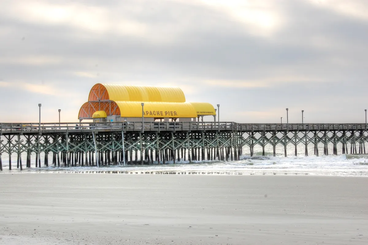 A serene view of the Apache Pier with its distinctive yellow roof extending over the water. The pier offers an iconic oceanfront experience, inviting guests for walks, fishing, or simply soaking in the sunrise and ocean air. The scene connects the condo’s location to Myrtle Beach’s celebrated attractions.