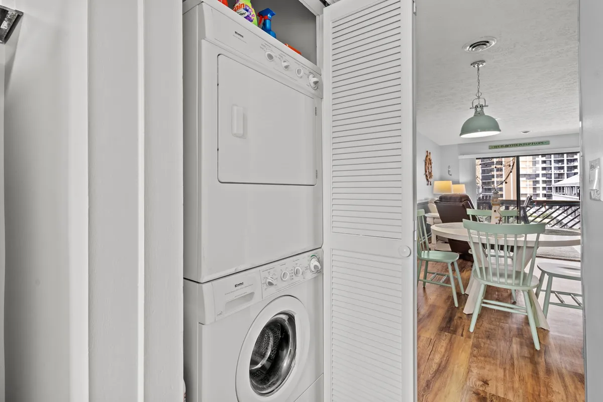 This image highlights the practical side of family stays, featuring a washer and dryer unit adjacent to a dining table with green chairs. The scene depicts people sharing laughter while folding laundry and enjoying meals together, blending functionality and comfort.