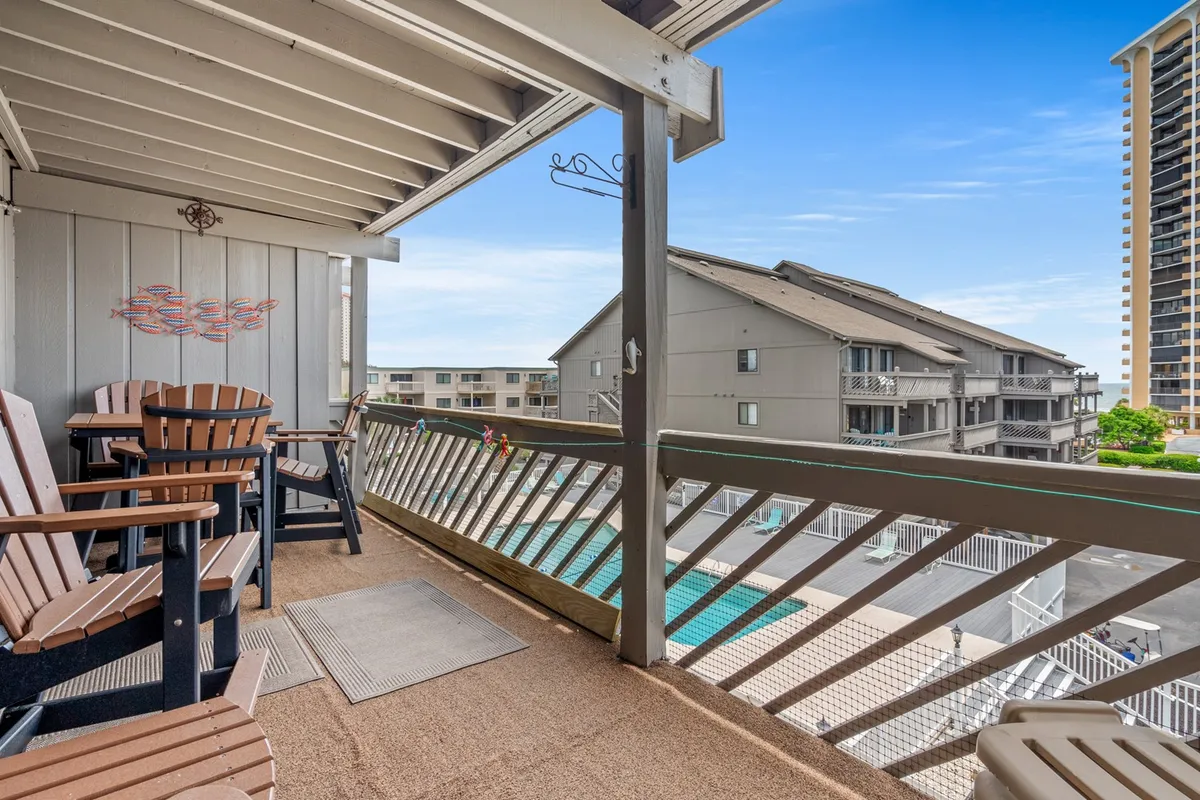 This image shows a well-appointed balcony with wooden chairs, a stylish railing, and decorative wall art. The balcony overlooks a sparkling pool, capturing both the tranquility of the private outdoor space and the resort amenities below.