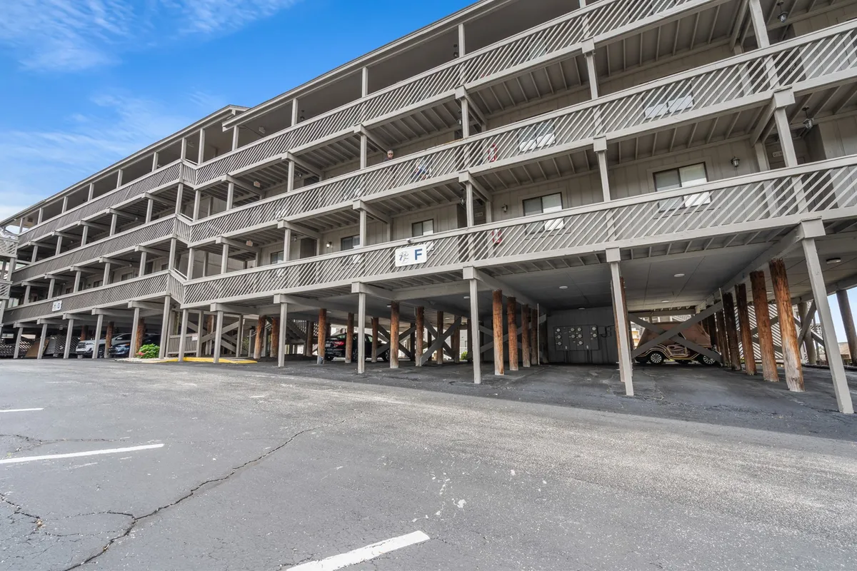 This exterior image shows the multi-level parking structure and several private balconies at Shipwatch Pointe. Exposed wooden beams give the complex a relaxed, beachy aesthetic. The balconies are visible, suggesting personal outdoor spaces for guests, while the parking area signals easy access for families or groups arriving by car.